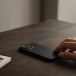 Main posée sur un téléphone à côté d’un carnet et d’un stylo